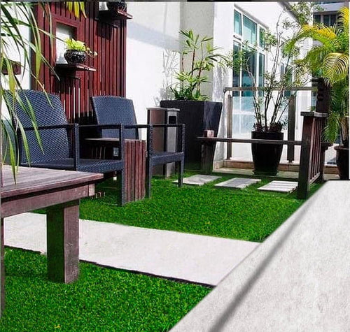 Outdoor patio scene with bright green artificial turf placed between concrete stepping stones and rattan chairs