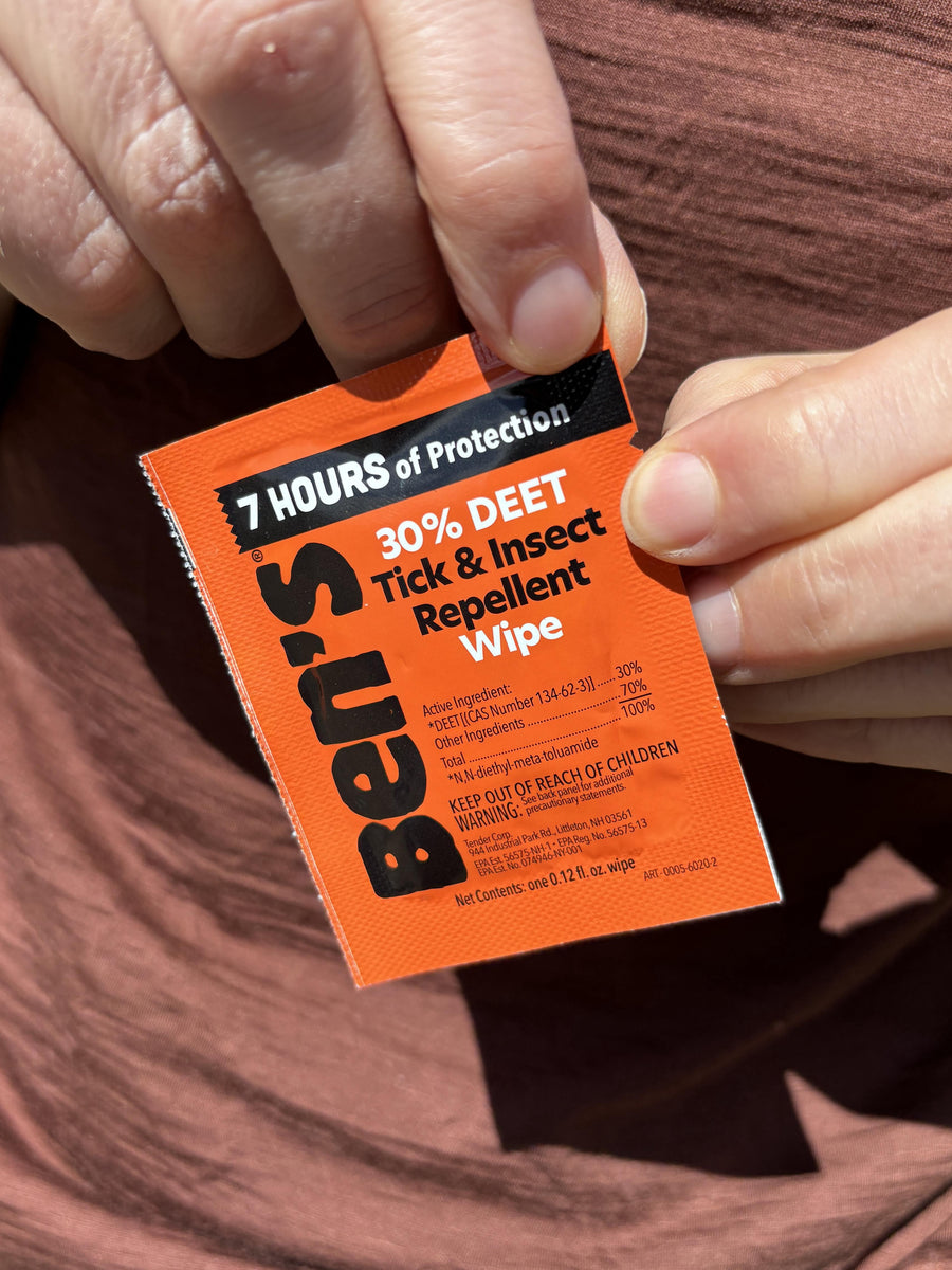 Close-up of hands holding an orange Ben's 30% DEET Tick & Insect Repellent single-use wipe packet outdoors