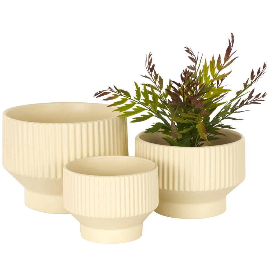 Three cream ceramic planters with vertical ribbed texture and tapered pedestal bases, one filled with faux greenery.