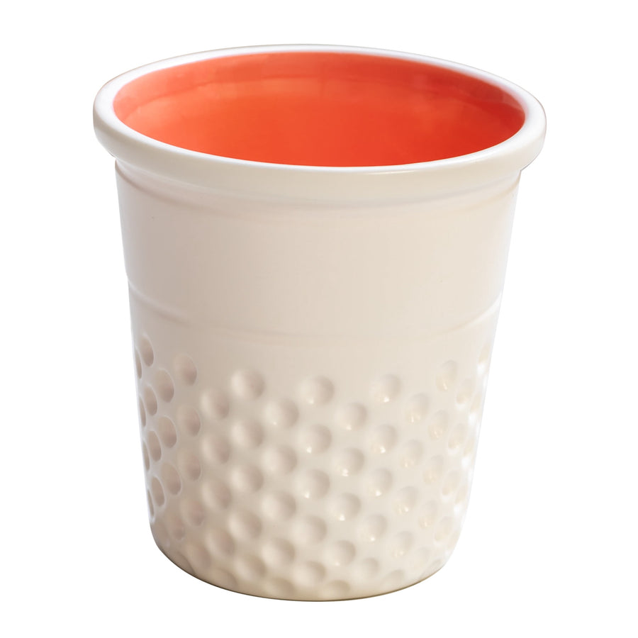 White ceramic thimble-shaped container with dimpled exterior and coral glazed interior, angled view