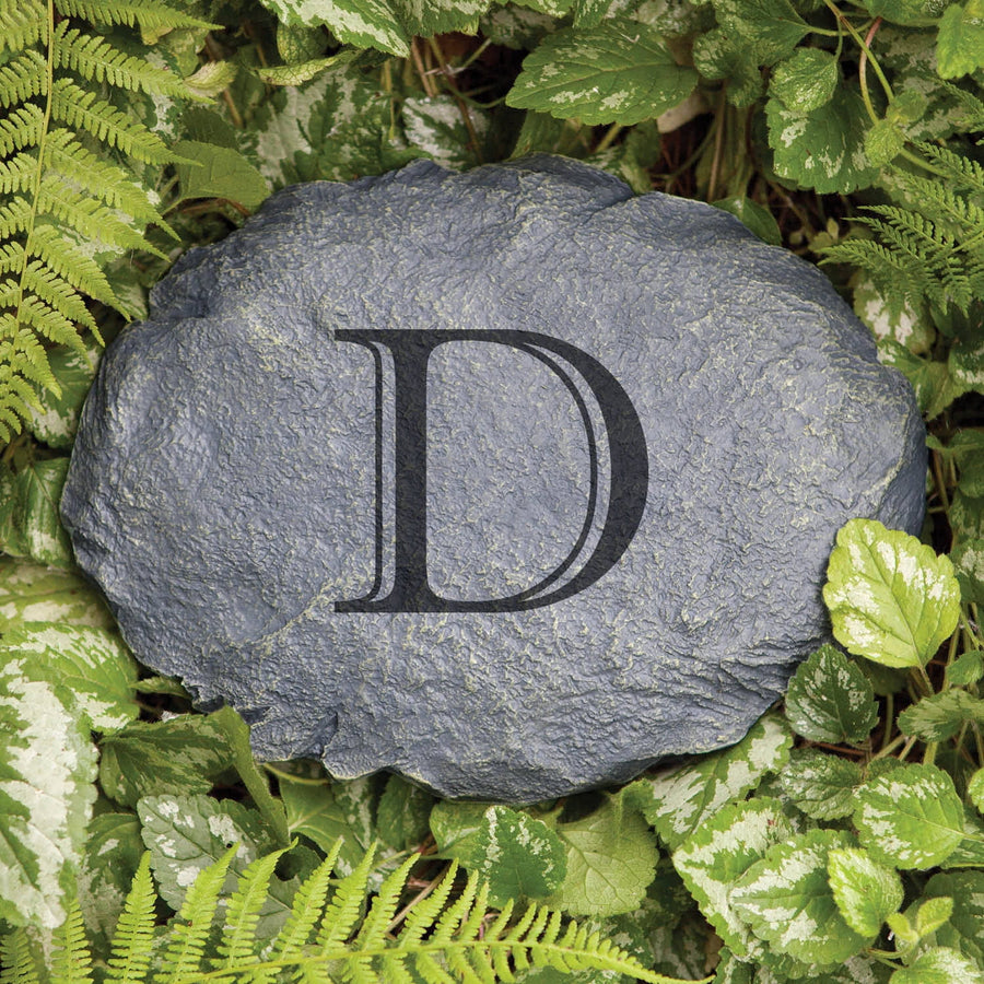 Oval faux-slate garden stone engraved with a large serif letter D, set among variegated green foliage.