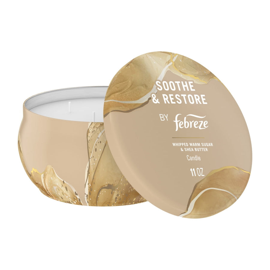 Open beige Febreze tin candle with lid propped to show white wax and four wicks, Soothe & Restore label