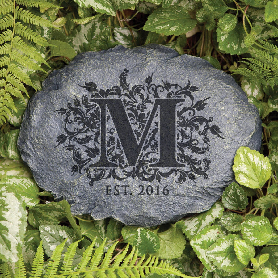Decorative garden stone with a large ornate letter M and “EST. 2016” surrounded by foliage