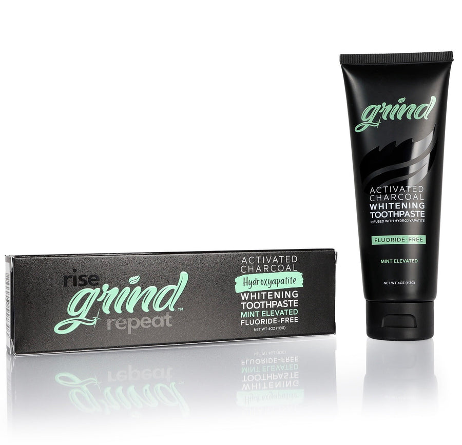 Black tube of Grind activated charcoal whitening toothpaste next to its black branded box on white reflective surface