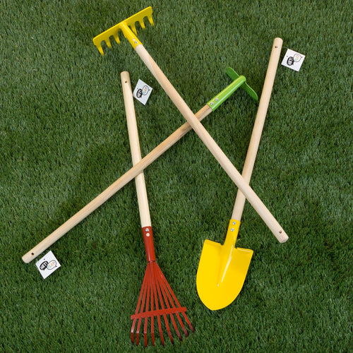 Four Hey! Play! children's garden tools with long wooden handles - yellow shovel, yellow rake, red leaf rake and green hoe - laid on grass.