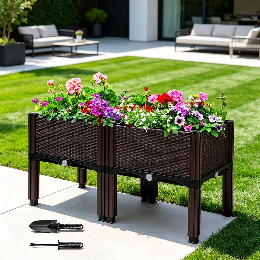 Woven-style elevated planter on legs filled with colorful flowering plants on a patio, small gardening trowel and fork beside it.