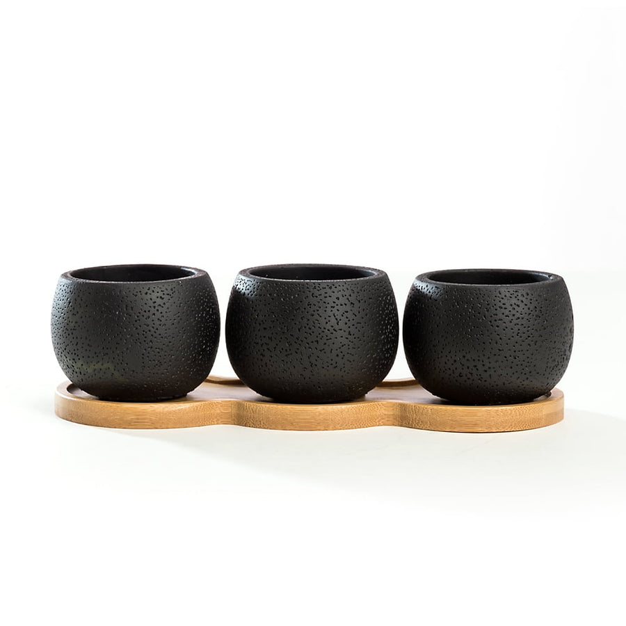 Three round textured black mini cement planters arranged on a contoured bamboo tray against white background.