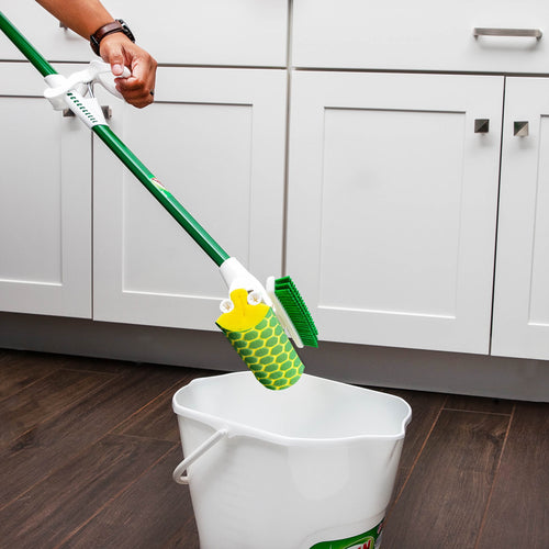 Green-handled sponge mop with scrub brush being wrung over a white bucket in a kitchen