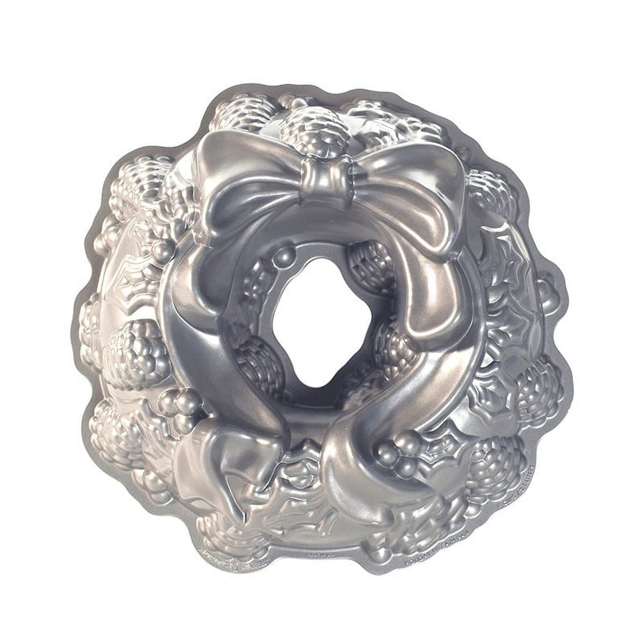 Shiny silver Nordic Ware holiday wreath bundt pan with bow and pinecone detail on white background
