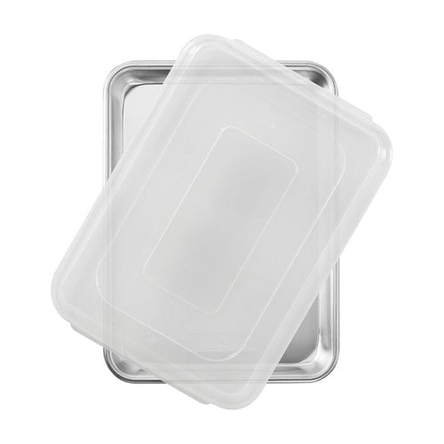 Overhead photo of a rectangular aluminum quarter sheet pan with a translucent plastic lid partially covering it on a white background.