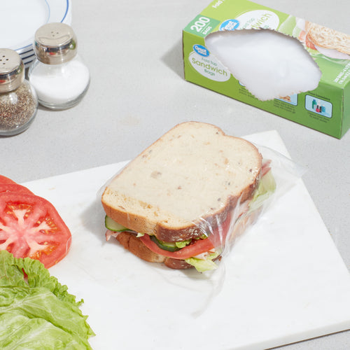 Prepared sandwich on a cutting board wrapped in a clear fold-top bag with a Great Value 200-count box in the background.