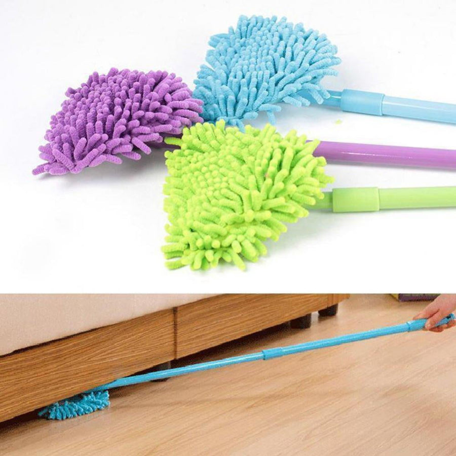 Close arrangement of three triangular microfiber mop heads and handles in blue, purple, and green with a person using a long handle to reach under furniture.