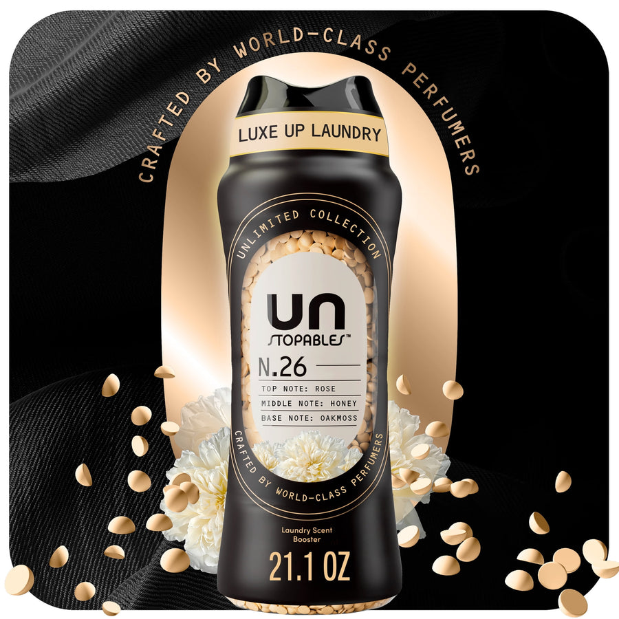 Black bottle of Unstopables N.26 scent booster surrounded by scattered beige beads and white flowers