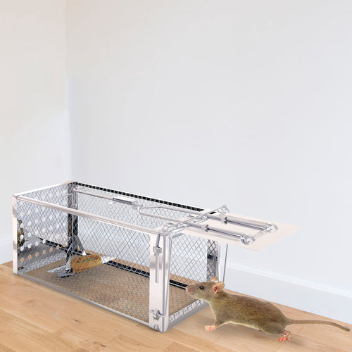 Stainless steel wire-mesh live-catch trap on a hardwood floor with a small mouse nearby and bait visible on the trap's pedal inside the cage.
