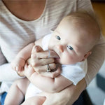 Adult holding an infant while using a clear silicone finger toothbrush on the baby's mouth in a lifestyle setting