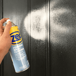 Aerosol can spraying white foam onto a dark paneled surface, nozzle aimed and cloud of foam visible.