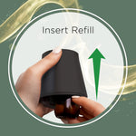 Instructional image showing hands inserting an amber refill into the black diffuser with an upward green arrow