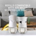 Blurry lifestyle image showing two Air Wick plug-in warmers on a table with overlaid text about compatibility with scented oil devices