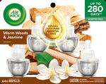 Package front showing four Air Wick Warm Woods & Jasmine scented oil refills with jasmine blossoms and wood background
