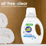 All free•clear fabric softener bottle staged on shelf next to rolled white towels against wood