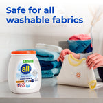 white tub of all free clear mighty pacs oxi detergent on a laundry counter with folded towels as a person folds a baby shirt; large text says safe for all washable fabrics