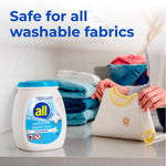 All Sensitive Fresh Mighty Pacs tub on a counter while a person folds a baby shirt, text claims safety for washable fabrics