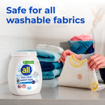 All free clear Mighty Pacs tub on a laundry counter with folded towels and hands holding a small baby shirt, safety text