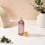 Stylistic scene of Allswell 'Relax' mauve spray bottle with wooden cap removed, placed on a marble surface with foliage props.