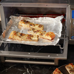 Sheet of aluminum foil lining a toaster oven tray with slices of baked pizza on top
