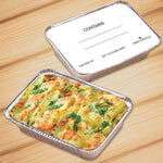 Two aluminum pans on wood surface, one filled with baked pasta and one topped with a writable board lid