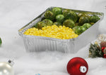 Aluminum takeout pan filled with corn and Brussels sprouts set on a white surface with holiday ornament decorations.
