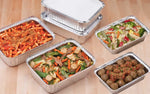 Several aluminum takeout pans displayed on a wooden surface filled with pasta, meatballs and vegetables, some with lids.