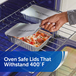 Aluminum tray of pasta and meatballs in an oven, hand lifting a labeled oven-safe folded lid