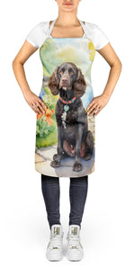 Person wearing an apron showing a brown American Water Spaniel seated in a vibrant spring garden scene