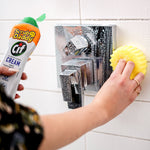 Hand applying Scrub Daddy Cif cream to a yellow scrubbing pad while cleaning a wet chrome shower control