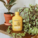 Yellow Arber insecticide bottle staged on a wooden shelf among potted houseplants and trailing foliage