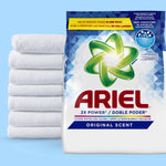 Close-up of an Ariel laundry powder bag beside a stack of white folded towels against a light blue background.