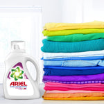 Ariel Ultra Concentrado detergent bottle next to a colorful folded laundry stack in a bright room with window light.