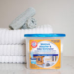 Arm & Hammer moisture absorber tub placed on a countertop beside folded towels in a styled laundry scene