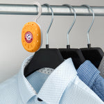 Arm & Hammer orange Closet Mate deodorizer hanging from a closet rod beside several shirt hangers in a wardrobe setting