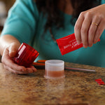 Hands assembling the red RESCUE fruit fly trap and pouring attractant liquid from a packet into the base cup