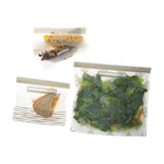 Three reusable zipper bags shown with sandwich, dried fruit and a large salad, each bag featuring a gray patterned design and gray zipper.