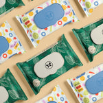 Multiple Honest flushable wipe packets in colorful and green leaf packaging arranged on a beige background