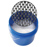 Blue plastic wash bucket filled with suds and a black removable grit guard partially lifted above the rim