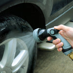 Hand holding Auto Drive gray and black nozzle spraying water at a car tire and rim