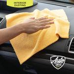 Hand dusting a car dashboard with a yellow Auto Drive microfiber towel with interior dash visible