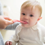 Close-up of a baby having their mouth brushed with a pink toddler toothbrush held by an adult hand.