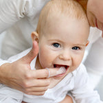 Adult using a silicone finger brush to gently clean a baby’s teeth while the baby opens mouth