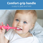 Baby holding and mouthing a pink elephant-design training toothbrush, showing the comfort-grip handle with promotional text above.