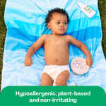 Baby lying on a blue striped towel outdoors with a Hello Bello mosquito repellent bottle visible near the top edge.